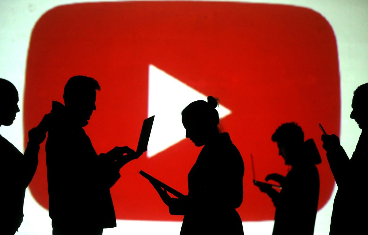 Silhouettes of laptop and mobile device users are seen next to a screen projection of Youtube logo in this picture illustration taken March 28, 2018.  REUTERS/Dado Ruvic/Illustration/ File Photo