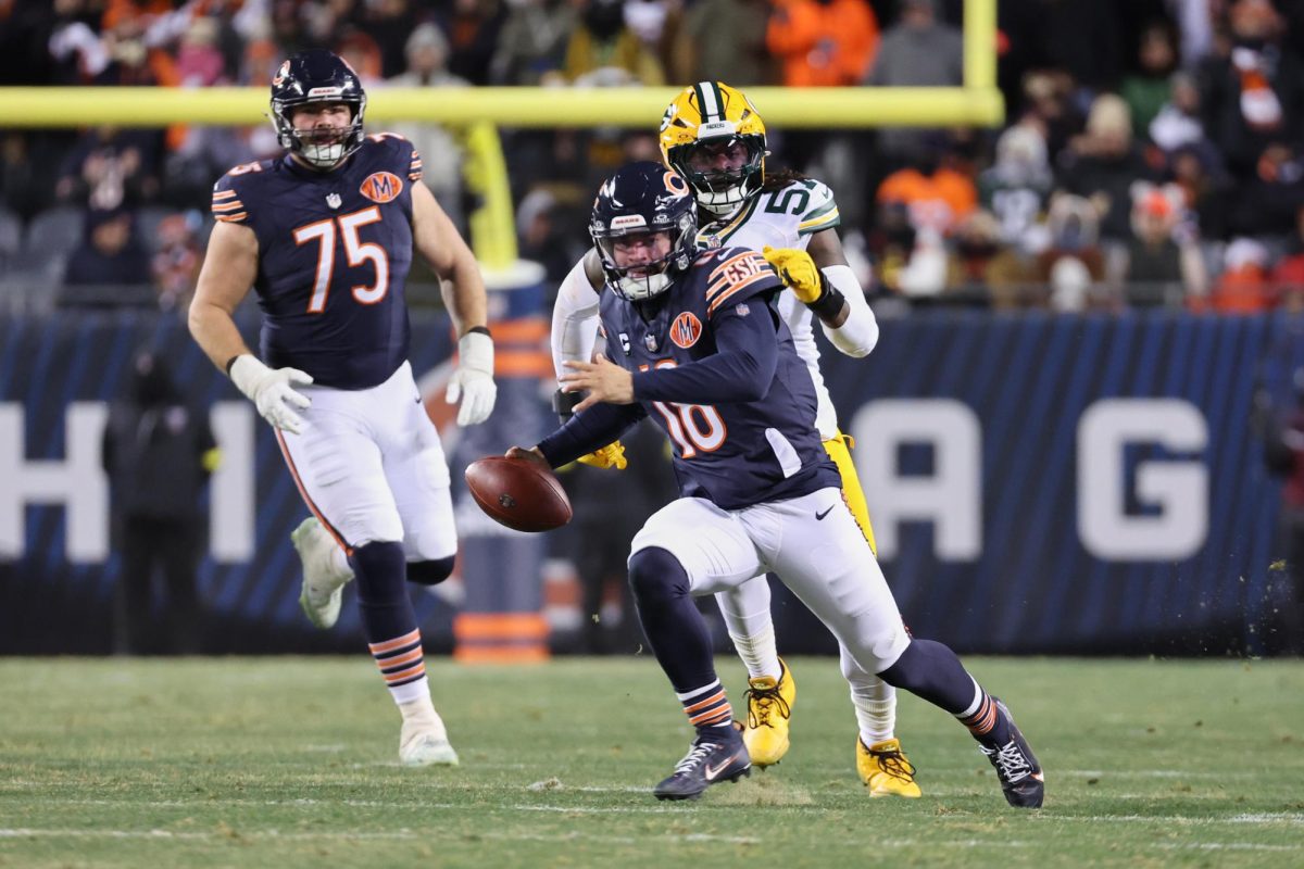 Dec 20, 2025; Chicago, Illinois, USA; Chicago Bears quarterback Caleb Williams (18) runs with the ball and offensive tackle Ozzy Trapilo (75) watches the play against Green Bay Packers defensive end Brenton Cox Jr. (57) during overtime at Soldier Field. Mandatory Credit: Mike Dinovo-Imagn Images